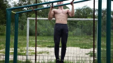 Genç kaslı sporcu spor alanında barfiks çekiyor. Atletik adam dışarıda egzersiz yapıyor. Yaz doğasında spor yapan güçlü bir adam. Sağlıklı ve aktif yaşam tarzı kavramı. Yavaş çekim
