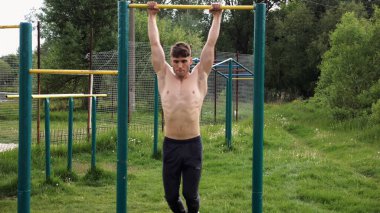 Spor sahasında barfiks çeken kaslı bir sporcu. Genç üstsüz sporcu doğada egzersiz yapıyor. Güçlü sporcu adam dışarıda antrenman yapıyor. Sağlıklı ve aktif yaşam tarzı kavramı. Yavaş çekim