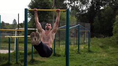 Atletik adam karın kaslarını eğitir spor sahasında yatay barda bacak kaldırır. Genç sporcu, barfiks çekme çubuğunda egzersiz yapıyor. Doğada spor yapan sporcu. Sağlıklı yaşam tarzı.