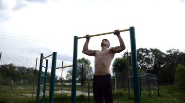 Spor sahasında barfiks çeken kaslı bir sporcu. Genç üstsüz sporcu doğada egzersiz yapıyor. Güçlü sporcu adam dışarıda antrenman yapıyor. Sağlıklı ve aktif yaşam tarzı kavramı. Yavaş çekim