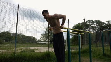 Genç sporcu doğada paralel barlarda şınav çekiyor. Spor alanında egzersiz yapan güçlü bir sporcu. Erkek üstsüz sporcu dışarıda sıkı çalışıyor. Aktif spor yaşam tarzı kavramı. Yavaş çekim
