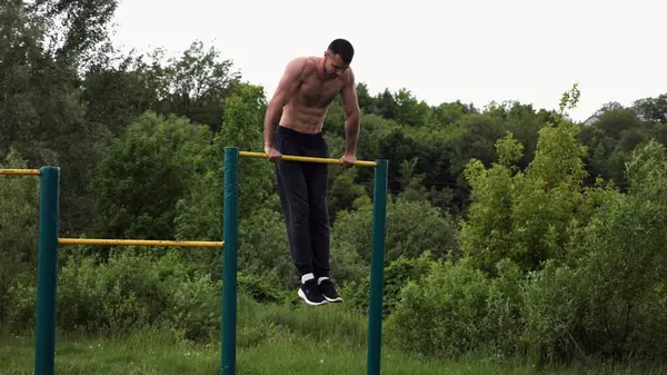 Cesur üstsüz sporcu doğada yatay çıtada şınav çekiyor. Güçlü ve kaslı adam spor alanında antrenman yapıyor. Genç atletik adam dışarıda egzersiz yapıyor. Aktif ve sağlıklı yaşam tarzı kavramı.
