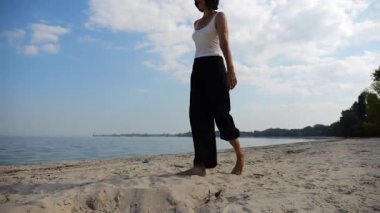 Güneşli bir günde sahilde kumsala giden mutlu yetişkin kadın. Arka planda sakin dalgalarla deniz kıyısında yürüyen güzel bir bayan. Yaz tatili ya da tatil kavramı. Yavaş çekim