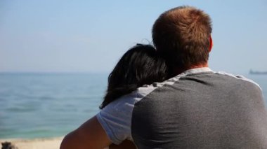 Kumsalda tahta kütüğün üzerinde otururken mutlu çift kucaklaşması. Güneşli bir günde deniz manzarasına hayran olan romantik bir çift. Sevgililer tatil köyünde birlikte vakit geçirirler. Yaz tatili ya da tatil kavramı. Yavaş çekim