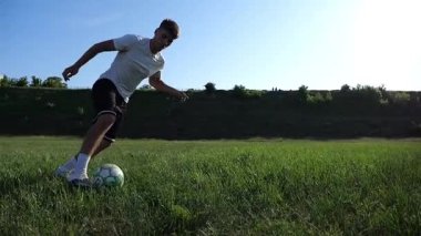 Üniformalı profesyonel futbolcu yeşil sahada koşarken topa numara yapıyor. Sporcu güneşli bir günde Meadow 'da koşarken topa vurur. Stadyumda antrenman yapan genç adam. Serbest stil futbol.