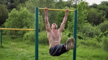 Atletik adam karın kaslarını eğitir spor sahasında yatay barda bacak kaldırır. Genç sporcu, barfiks çekme çubuğunda egzersiz yapıyor. Doğada spor yapan sporcu. Sağlıklı yaşam tarzı.