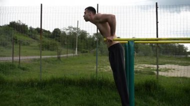 Genç sporcu doğada paralel barlarda şınav çekiyor. Spor alanında egzersiz yapan güçlü bir sporcu. Erkek üstsüz sporcu dışarıda sıkı çalışıyor. Aktif spor yaşam tarzı kavramı. Yavaş çekim