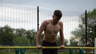 Erkek üstsüz sporcu doğada paralel barlarda şınav çekiyor. Spor alanında egzersiz yapan güçlü bir sporcu. Genç sporcu dışarıda sıkı çalışıyor. Aktif spor yaşam tarzı kavramı. Yavaş çekim