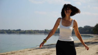 Güneşli bir günde sahil kenarında kumsalda yürüyen güzel bir bayan. Mutlu yetişkin kadın kıyı şeridine doğru dönüyor. Kaygısız kadın deniz kenarında dinleniyor. Yaz tatili veya tatil kavramı.