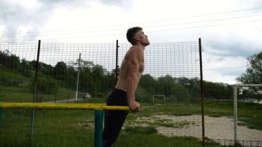 Genç sporcu doğada paralel barlarda şınav çekiyor. Spor alanında egzersiz yapan güçlü bir sporcu. Erkek üstsüz sporcu dışarıda sıkı çalışıyor. Aktif spor yaşam tarzı kavramı. Yavaş çekim