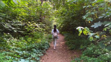 Genç bir kadın yaz ormanında patika boyunca gidiyor. Sırt çantalı bir kadın vahşi doğada patikaların arasında yürüyor. Tanınmayan bir kız dışarıda gezmekten zevk alıyor. Manzaraya hayran kalıyor. Kapat.