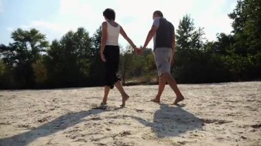 Romantik çift el ele tutuşup kumsalda yürüyor. Güneşli bir günde kıyıya giden mutlu bir çift. Sevgililer tatil köyünde birlikte vakit geçirirler. Yaz tatili veya tatil kavramı.