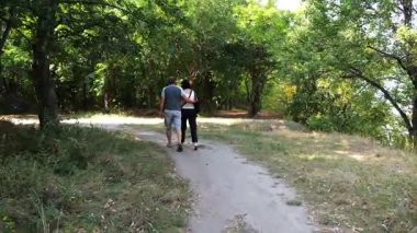 Mutlu çift yaz ormanında yolda yürüyor. Vahşi ormanlık alanda romantik bir çift geziyor. Sevgililer doğada birlikte vakit geçirirler. Aşk ve mutluluk kavramı. Yavaş çekim