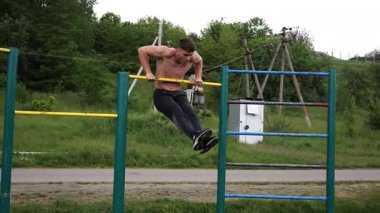Güçlü ve kaslı bir adam doğanın yatay çubuğunda egzersiz yapıyor. Spor sahasında sıkı gömleksiz sporcu. Genç atletik adam dışarıda egzersiz yapıyor. Sağlıklı yaşam tarzı kavramı.
