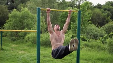 Atletik adam karın kaslarını eğitir spor sahasında yatay barda bacak kaldırır. Genç sporcu, barfiks çekme çubuğunda egzersiz yapıyor. Doğada spor yapan sporcu. Sağlıklı yaşam tarzı.