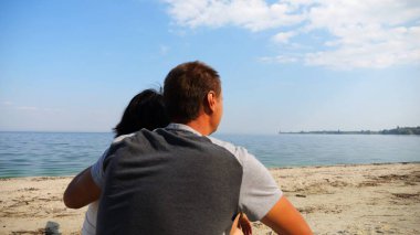 Kumsalda tahta kütüğün üzerinde otururken mutlu çift kucaklaşması. Güneşli bir günde deniz manzarasına hayran olan romantik bir çift. Sevgililer tatil köyünde birlikte vakit geçirirler. Yaz tatili ya da tatil kavramı. Yavaş çekim