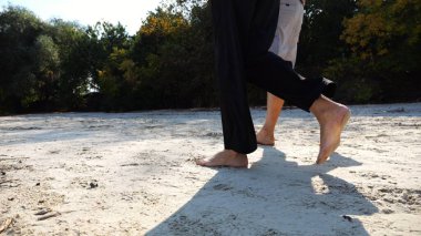 Çiftin erkek ve dişi bacakları kumlu sahilde yürüyor. Güneşli bir günde kumsalda yürüyen çıplak ayaklı bir çift. Sevgililer tatil köyünde birlikte vakit geçirirler. Yaz tatili veya tatil kavramı.