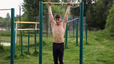 Spor sahasında barfiks çeken kaslı bir sporcu. Genç üstsüz sporcu doğada egzersiz yapıyor. Güçlü sporcu adam dışarıda antrenman yapıyor. Sağlıklı ve aktif yaşam tarzı kavramı. Yavaş çekim