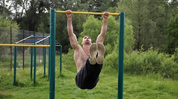 Atletik adam karın kaslarını eğitir spor sahasında yatay barda bacak kaldırır. Genç sporcu, barfiks çekme çubuğunda egzersiz yapıyor. Doğada spor yapan sporcu. Sağlıklı yaşam tarzı.