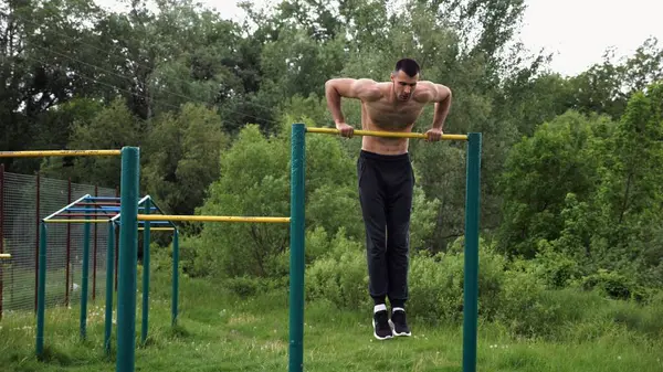 Cesur üstsüz sporcu doğada yatay çıtada şınav çekiyor. Güçlü ve kaslı adam spor alanında antrenman yapıyor. Genç atletik adam dışarıda egzersiz yapıyor. Aktif ve sağlıklı yaşam tarzı kavramı.