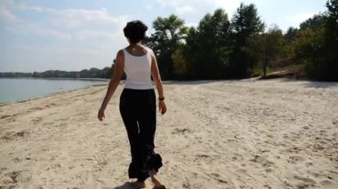 Güneşli bir günde sahilde koşan mutlu yetişkin kadın. Arka planda sakin dalgalarla deniz kıyısında koşan güzel bir bayan. Yaz tatili ya da tatil kavramı. Yavaş çekim