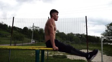 Güçlü bir adam karın kaslarını eğitir spor sahasında paralel barlarda bacak kaldırır. Genç üstsüz sporcu doğada egzersiz yapıyor. Doğada spor yapan sporcu. Sportif yaşam tarzı kavramı