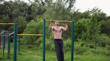 Güçlü ve kaslı bir adam doğanın yatay çubuğunda egzersiz yapıyor. Spor sahasında sıkı gömleksiz sporcu. Genç atletik adam dışarıda egzersiz yapıyor. Sağlıklı yaşam tarzı kavramı