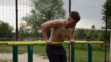 Erkek üstsüz sporcu doğada paralel barlarda şınav çekiyor. Spor alanında egzersiz yapan güçlü bir sporcu. Genç sporcu dışarıda sıkı çalışıyor. Aktif spor yaşam tarzı kavramı. Yavaş çekim