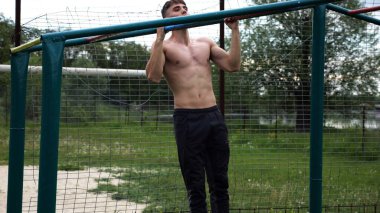Genç kaslı sporcu spor alanında barfiks çekiyor. Atletik adam dışarıda egzersiz yapıyor. Yaz doğasında spor yapan güçlü bir adam. Sağlıklı ve aktif yaşam tarzı kavramı. Yavaş çekim