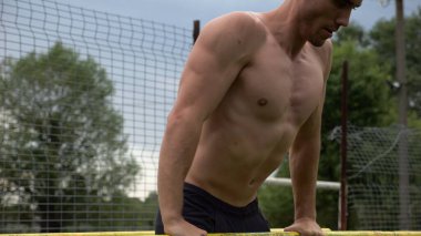 Erkek üstsüz sporcu doğada paralel barlarda şınav çekiyor. Spor alanında egzersiz yapan güçlü bir sporcu. Genç sporcu dışarıda sıkı çalışıyor. Aktif spor yaşam tarzı kavramı. Yavaş çekim