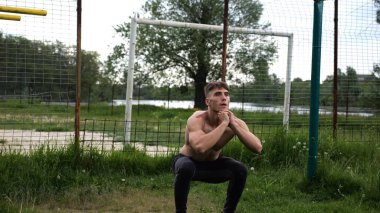 Spor sahasında çömelme hareketleri yapan erkek üstsüz atlet. Yaz doğasında çalışan genç bir sporcu. Güçlü sporcu dışarıda egzersiz yapıyor. Aktif ve sportif yaşam tarzı kavramı. Yavaş çekim