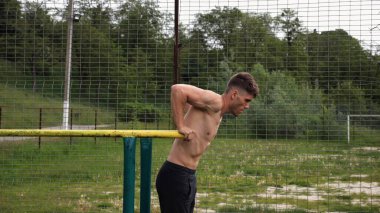 Genç sporcu doğada paralel barlarda şınav çekiyor. Spor alanında egzersiz yapan güçlü bir sporcu. Erkek üstsüz sporcu dışarıda sıkı çalışıyor. Aktif spor yaşam tarzı kavramı. Yavaş çekim