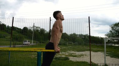 Genç sporcu doğada paralel barlarda şınav çekiyor. Spor alanında egzersiz yapan güçlü bir sporcu. Erkek üstsüz sporcu dışarıda sıkı çalışıyor. Aktif spor yaşam tarzı kavramı. Yavaş çekim