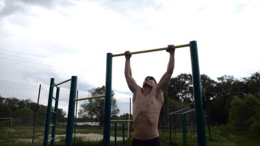 Spor sahasında barfiks çeken kaslı bir sporcu. Genç üstsüz sporcu doğada egzersiz yapıyor. Güçlü sporcu adam dışarıda antrenman yapıyor. Sağlıklı ve aktif yaşam tarzı kavramı. Yavaş çekim