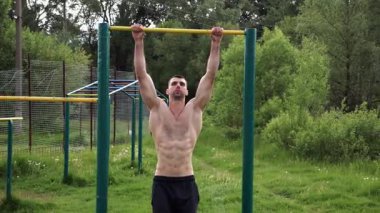 Atletik adam karın kaslarını eğitir spor sahasında yatay barda bacak kaldırır. Genç sporcu, barfiks çekme çubuğunda egzersiz yapıyor. Doğada spor yapan sporcu. Sağlıklı yaşam tarzı.