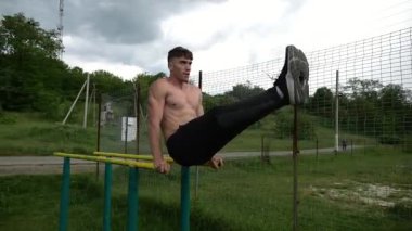 Güçlü bir adam karın kaslarını eğitir spor sahasında paralel barlarda bacak kaldırır. Genç üstsüz sporcu doğada egzersiz yapıyor. Doğada spor yapan sporcu. Sportif yaşam tarzı kavramı.