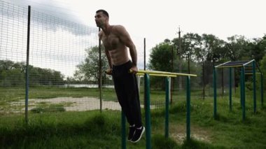 Genç sporcu doğada paralel barlarda şınav çekiyor. Spor alanında egzersiz yapan güçlü bir sporcu. Erkek üstsüz sporcu dışarıda sıkı çalışıyor. Aktif spor yaşam tarzı kavramı. Yavaş çekim