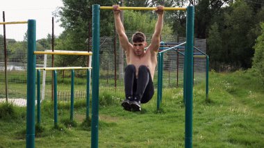 Spor sahasında karın kaslarını çalıştıran güçlü bir adam. Genç sporcu, barfiks çekme çubuğunda egzersiz yapıyor. Doğada spor yapan sporcu. Sportif yaşam tarzı kavramı.