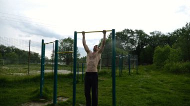 Spor sahasında barfiks çeken kaslı bir sporcu. Genç üstsüz sporcu doğada egzersiz yapıyor. Güçlü sporcu adam dışarıda antrenman yapıyor. Sağlıklı ve aktif yaşam tarzı kavramı. Yavaş çekim