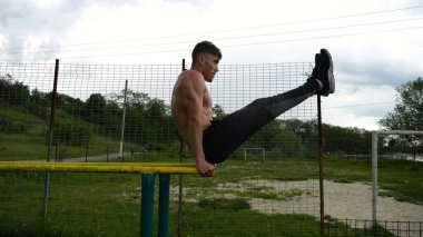 Güçlü bir adam karın kaslarını eğitir spor sahasında paralel barlarda bacak kaldırır. Genç üstsüz sporcu doğada egzersiz yapıyor. Doğada spor yapan sporcu. Sportif yaşam tarzı kavramı.