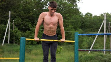 Cesur üstsüz sporcu doğada yatay çıtada şınav çekiyor. Güçlü ve kaslı adam spor alanında antrenman yapıyor. Genç atletik adam dışarıda egzersiz yapıyor. Aktif ve sağlıklı yaşam tarzı kavramı.