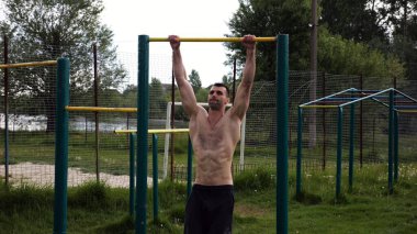 Spor sahasında barfiks çeken kaslı bir sporcu. Genç üstsüz sporcu doğada egzersiz yapıyor. Güçlü sporcu adam dışarıda antrenman yapıyor. Sağlıklı ve aktif yaşam tarzı kavramı. Yavaş çekim