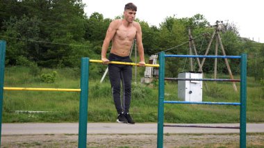 Cesur üstsüz sporcu doğada yatay çıtada şınav çekiyor. Güçlü ve kaslı adam spor alanında antrenman yapıyor. Genç atletik adam dışarıda egzersiz yapıyor. Aktif ve sağlıklı yaşam tarzı kavramı.