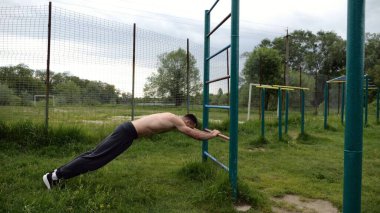 Spor malzemelerinde trisepsler üzerinde egzersiz yapan genç kaslı bir atlet. Spor alanında spor yapan erkek üstsüz bir sporcu. Doğada güçlü bir sporcu eğitimi. Sağlıklı yaşam tarzı kavramı.