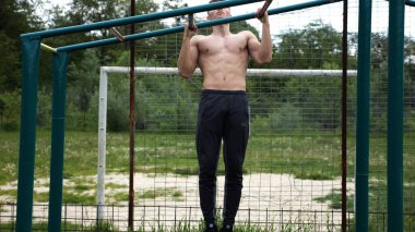 Genç kaslı sporcu spor alanında barfiks çekiyor. Atletik adam dışarıda egzersiz yapıyor. Yaz doğasında spor yapan güçlü bir adam. Sağlıklı ve aktif yaşam tarzı kavramı. Yavaş çekim