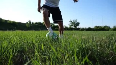 Profesyonel futbolcunun erkek ayağı, yeşil sahada koşarken topla numaralar gösterir. Güneşli bir günde Meadow 'da koşan sporcu bacakları topa vurur. Stadyumda antrenman yapan genç adam. Yavaş çekim