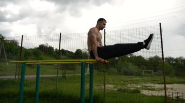 Güçlü bir adam karın kaslarını eğitir spor sahasında paralel barlarda bacak kaldırır. Genç üstsüz sporcu doğada egzersiz yapıyor. Doğada spor yapan sporcu. Sportif yaşam tarzı kavramı.