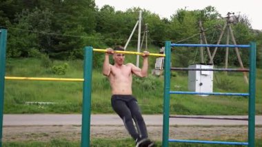 Güçlü ve kaslı bir adam doğanın yatay çubuğunda egzersiz yapıyor. Spor sahasında sıkı gömleksiz sporcu. Genç atletik adam dışarıda egzersiz yapıyor. Sağlıklı yaşam tarzı kavramı.