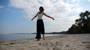 Güneşli bir günde sahil kenarında kumsalda yürüyen güzel bir bayan. Mutlu yetişkin kadın kıyı şeridine doğru dönüyor. Kaygısız kadın deniz kenarında dinleniyor. Yaz tatili veya tatil kavramı