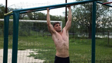 Genç kaslı sporcu spor alanında barfiks çekiyor. Atletik adam dışarıda egzersiz yapıyor. Yaz doğasında spor yapan güçlü bir adam. Sağlıklı ve aktif yaşam tarzı kavramı. Yavaş çekim